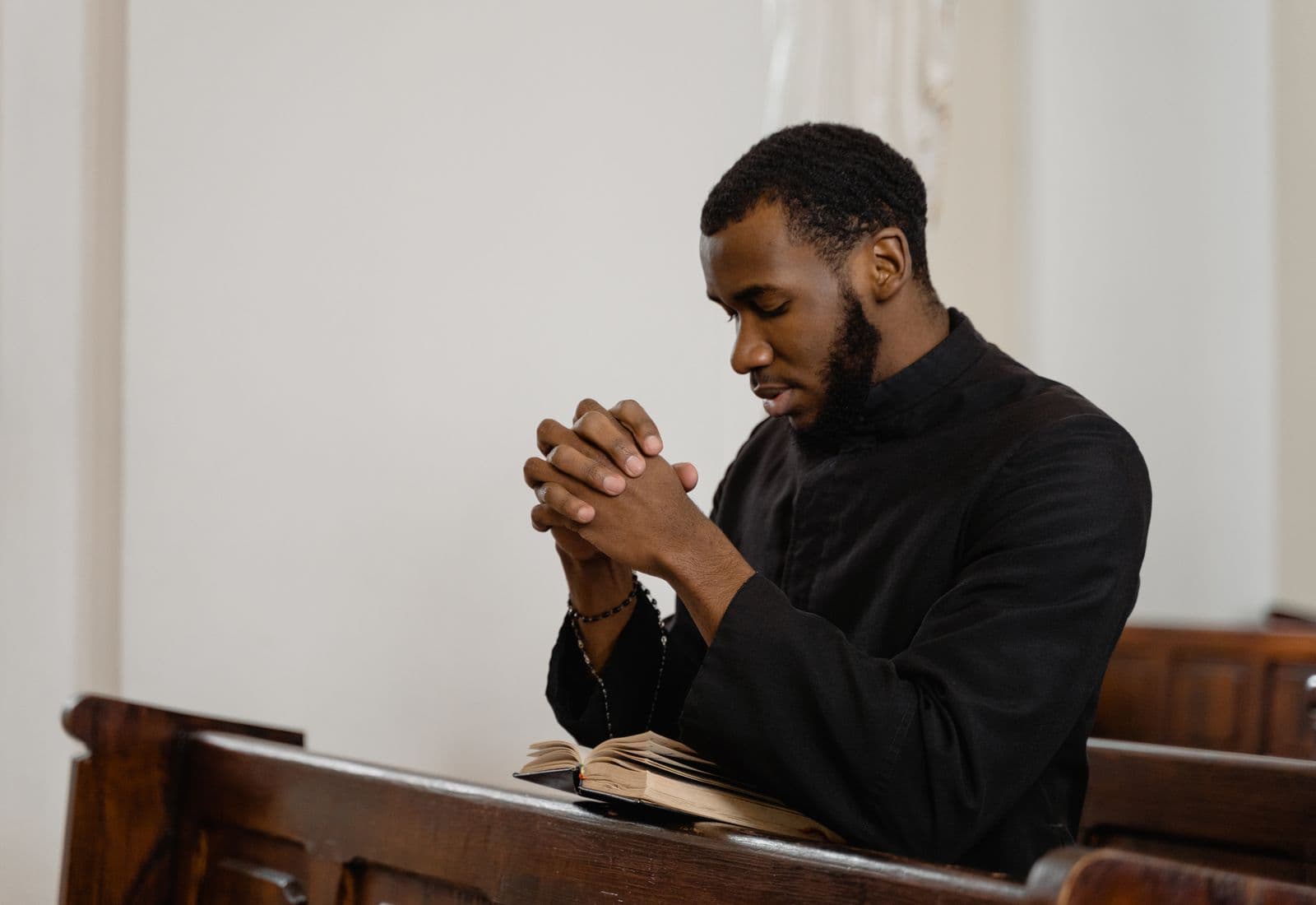 A man sitting alone in a church pew with his hands clasped and head bowed