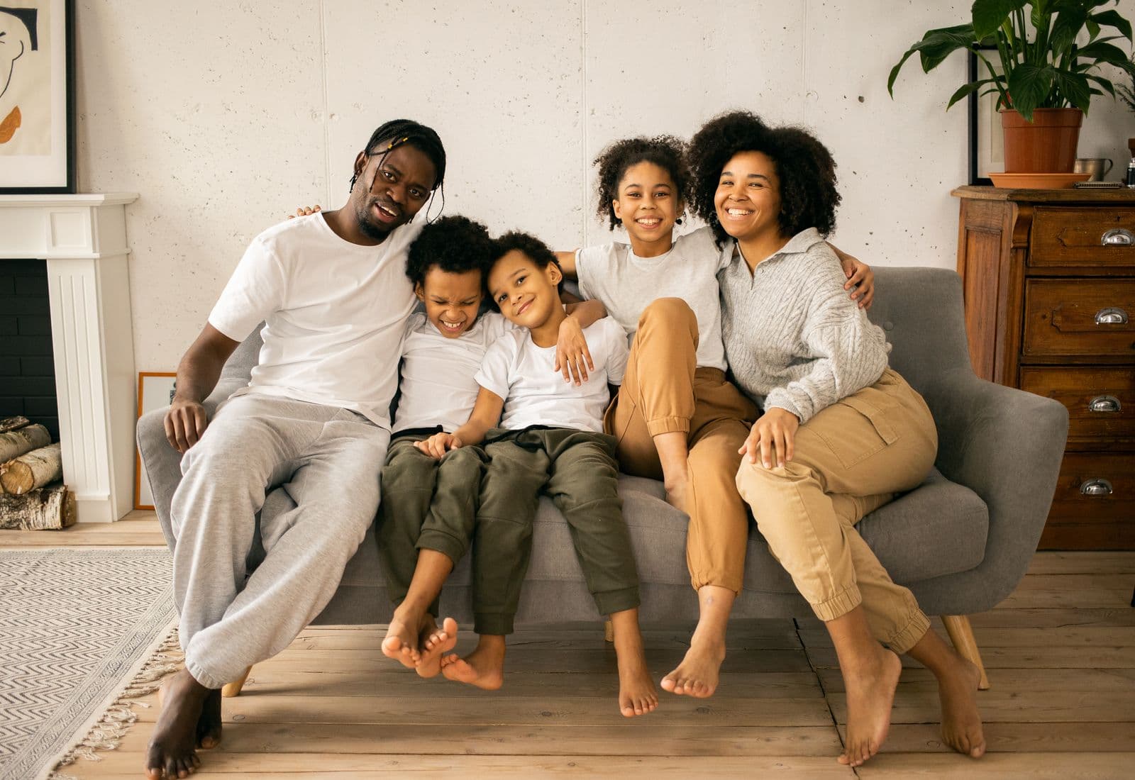 Two parents and three children sitting close together on a sofa at home, laughing
