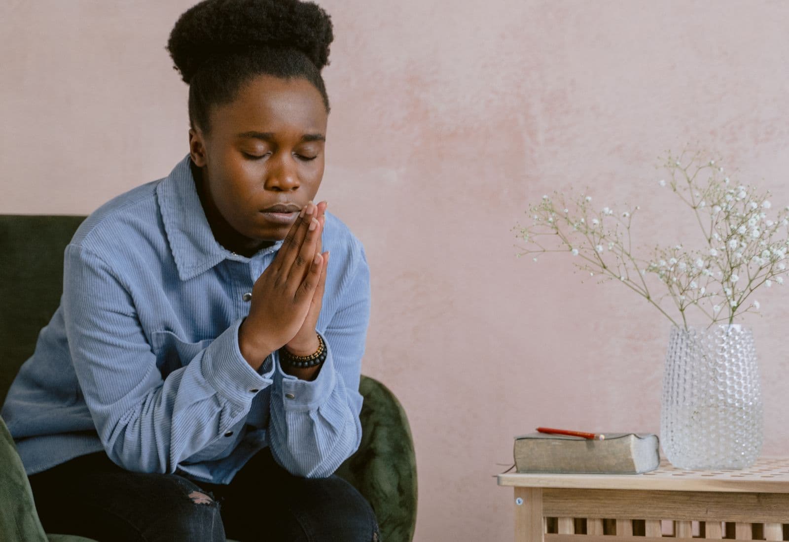 A young woman sitting quietly with her hands together, eyes closed, in a calm room