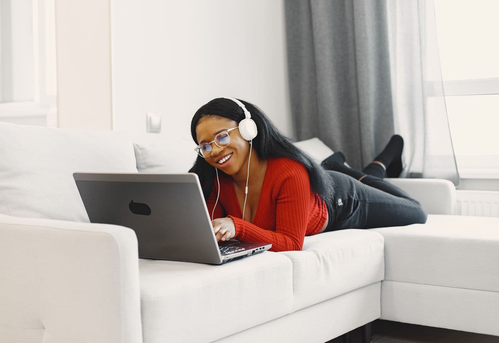 A woman wearing headphones, relaxed on a sofa at home during a video session on her laptop